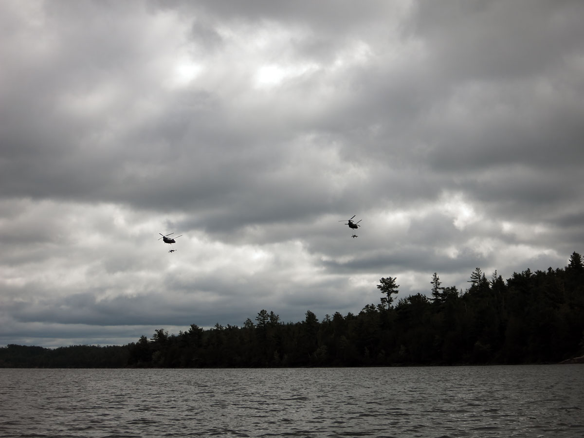 Two Chinook helicopters carrying artillery pieces over McManus Lake on the Petawawa River in Algonquin Park