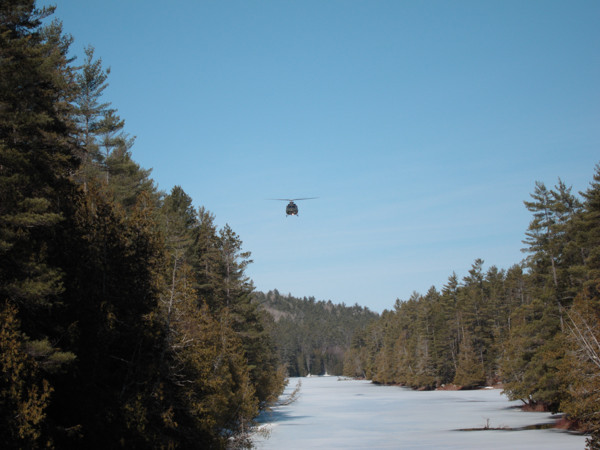 Army helicopter flying low over the frozen Barron River in Algonquin Park